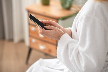 Obraz na płótnie Canvas A woman in a white bath robe texting on a smartphone