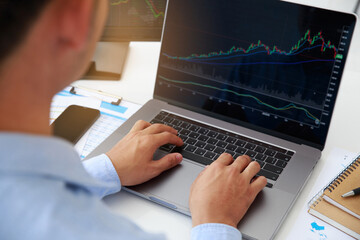  Close-up young businessman statistic graph of stock market financial indices analysis on a laptop and on a desktop computer in office. Analyzing and Trading Stock concept.