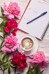 Morning coffee mug for breakfast, empty notebook, pencil and pink peony flowers on white stone table top view in flat lay style.
