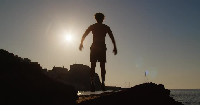 Sagoma di un ragazzo che si riscalda su uno scoglio vicino al mare