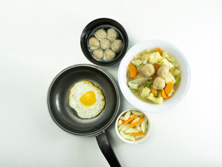 Omelet, pickled cucumber meatballs and meatball soup on a wooden cutting board on a white background.