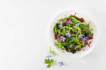 Mix salad with baby spinach, mizuna salad, bull's blood sprouts, edible flowers and olives on a white background, top view, place for text