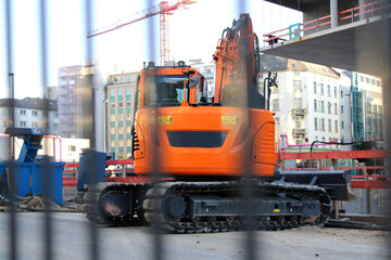 Orange crawler excavator on a construction site in the city centre behind a construction fence.