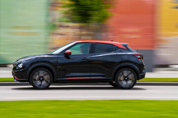 Side view of high speed luxury modern electric SUV car driving in the city streets. Blurred...