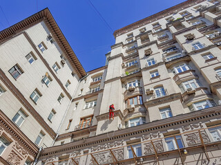 An industrial climber in a red uniform and with a safety net hangs on the wall of an old building