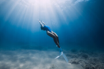 Female freediver with fins glide underwater in sea with sunlight. Summer freediving.