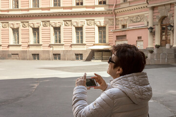 Elderly woman admires the architecture and chooses the angle for the photo. Female traveler on vacation takes photos.
