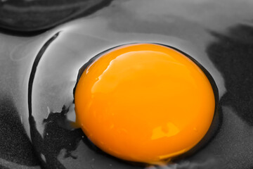 Bright round yolk among transparent white in a black frying pan. The concept of the process of preparing a simple dish for breakfast. Close-up