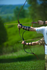 professional archers shooting with modern longbows at meadow