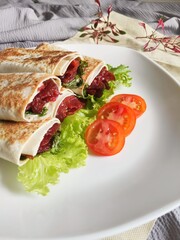 Kebab on White Plate. A delicious Kebab wrap with spicy meat, lettuce, tomato, and sauce. Selective Focus
