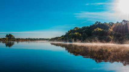 Aerial  view of a beautiful summer  landscape over river while dawn. Top view over river with a smooth water surface reflecting blue sky. Morning evaporation on a river while sunrise.