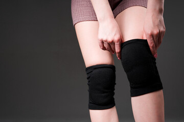 Photo of female hands. The girl pulls a black knee pad on her leg. Isolated on dark background © DmitryStock