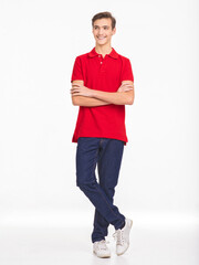 Fototapeta premium Photo of full length portrait of young happy smiling man isolated on a white background. Portrait of smiling handsome guy posing at studio. Attractive teenage boy in a red shirt and dark blue jeans