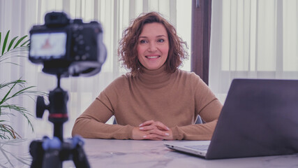 Smiling woman recording her video blog. Woman blogger videotapes her vlog at home.  Adult woman...