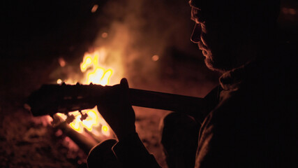 Man is playing guitar by the campfire in nature. Weekend in nature by the fire. Adult man is...