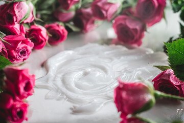 White cream, smeared on glossy surface surrounded by blurred delicate pink roses