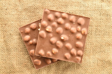 Two bars of dark chocolate with nuts on a jute napkin, close-up, top view.