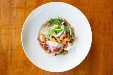 Vermicelli spicy salad with seafood and cashew in white dish on wooden table.