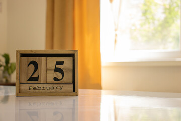 Wooden blocks of the calendar represents the date 25 and the month of February on the background of a window, curtain and a plant