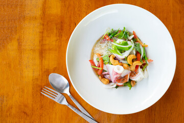 Vermicelli spicy salad with seafood and cashew in white dish on wooden table.