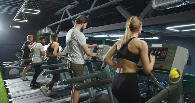Cropped view of the young man in sportswear started running on treadmill at the gym with a lot of people at the background. Stock video