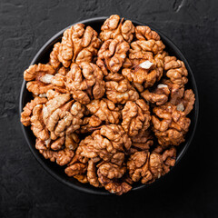 Peeled walnuts in a bowl on a black textured background, top view.