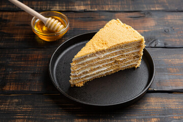 Slice of layered honey cake on dark wooden background