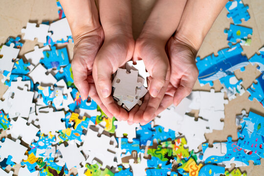 Mother and child hand holding jigsaw puzzle. Home puzzle game. Autism awareness. Mental health care concept with jigsaw pattern supported by family caregiver parent. Family and parent concept - Powered by Adobe
