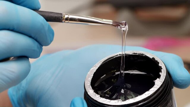 Close-up. The manicurist picks up the gel with a brush before applying it to the nails. The preparation process before applying shellac in a beauty salon. Preparation for applying acrylic to the nails