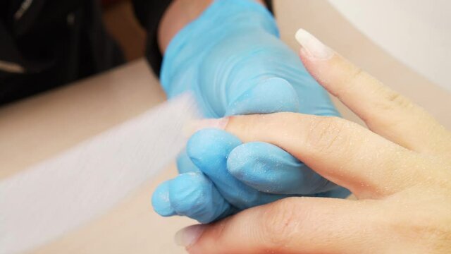 Manicurist files the shape of the nails with a special nail file, close up view. The manicurist shapes the nails with a nail file. The process of nail care in a beauty salon. Nail file processing.