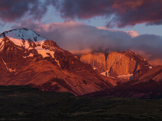 Fototapeta na wymiar Red Sunset in the Andes Mountains. Landscape with Morning Andes, Chile. Top of the Mount Torres del Paine Covered by Clouds. Snow Lying on the Slope of the Mountain.