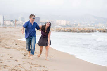 young beautiful and happy mixed ethnicity couple of Asian woman and Caucasian man relaxed and cheerful walking playful  on beach enjoying love and romantic holidays