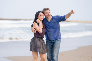 young beautiful and happy mixed ethnicity couple of Asian woman and Caucasian man relaxed and cheerful walking playful  on beach enjoying love and romantic holidays