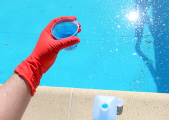 Blue liquid in a plastic glass for cleaning and clarity of water in swimming pools. Liquid algicide. Chemical agent for algae Water purification.