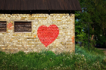 Graffiti painted big red heart on yellow brick building wall surrounded by grass and trees