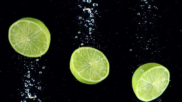 Lime splashing into the water in slow motion. Three halves of limes falling slowly on a black background. Organic green citrus isolated on black background. Fresh water with fruits.