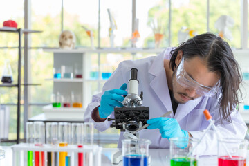 Young Asian smart man scientist is looking through microsocpe in laboratory.