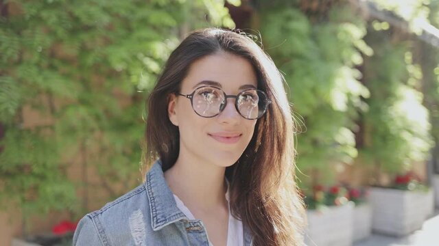 Great weather. Portrait view of the brunette cute woman wearing glasses standing at the summer street and looking at the camera while walking and enjoying of the walking. Stock video