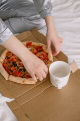 Fresh pizza in bed in the morning Female body in pajamas on the bed
