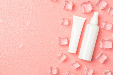 Top view photo of white cream tube and spray bottle without label ice cubes on the right and drops on isolated pastel pink background with copyspace on the left