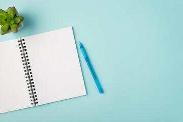 Top view photo of open notebook blue pen and plant on isolated pastel blue background with blank space