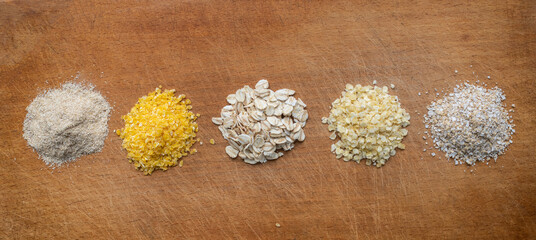 Oat flakes, corn flakes, millet flakes and two types of oat bran on a wooden board.