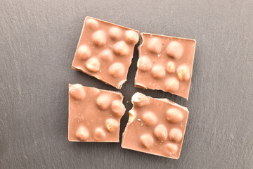 One broken bar of dark chocolate with nuts on a slate board, close-up, top view.
