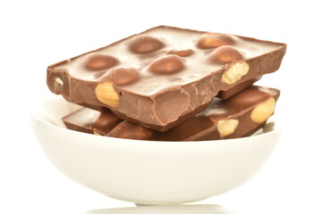 Several slices of dark chocolate with nuts on a white ceramic saucer, close-up, isolated on white.