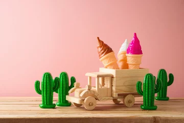Fototapete Summer holidays concept with toy truck, ice cream and cactus on wooden table over pink background. © maglara