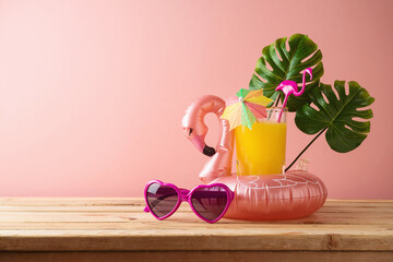 Summer tropical vacation concept with orange juice and flamingo pool float on wooden table over...