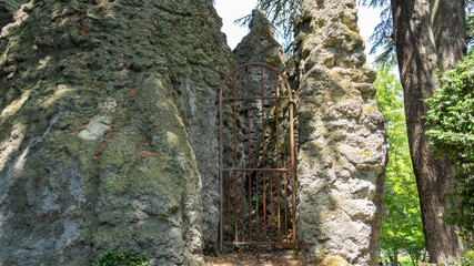 Red metal gate, arched top, between the rocks, closing the access to a waterfall