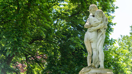 Pretty statues of a hugging couple, surrounded by trees and flowers