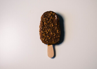 Ice cream in dark chocolate with nuts on a stick, on a white table
