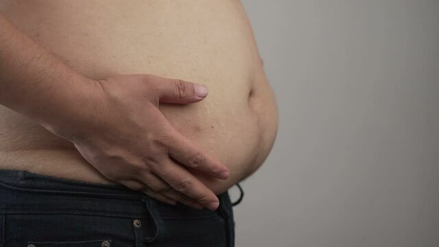 Close up of overweight man demonstrates a big belly with obesity. Hands of an obese man touching his fat tummy. slow motion of belly fat shake